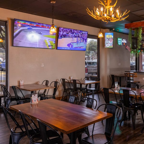 A restaurant dining area with wooden tables, black chairs, and multiple TVs showing sports.