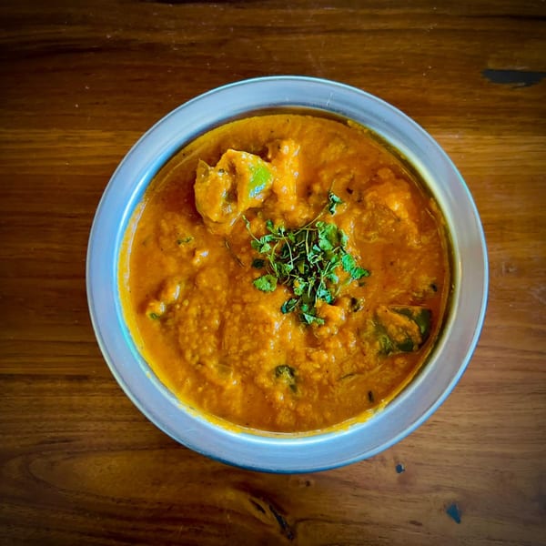 Close-up of a vibrant orange curry dish with green herbs in a metal bowl on a wooden table.