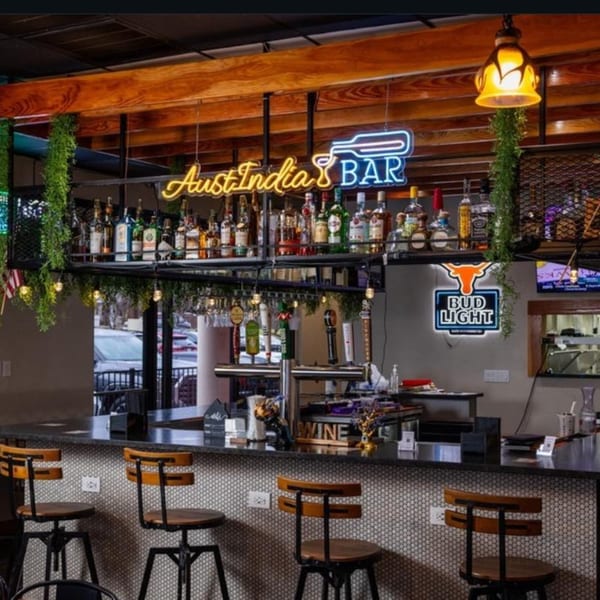 A well-stocked bar with neon signs, bar stools, and bottles of liquor under warm lighting.