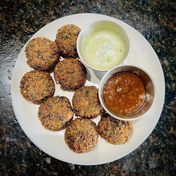A white plate holds eight round, crispy brown fritters and two small cups of dipping sauces.