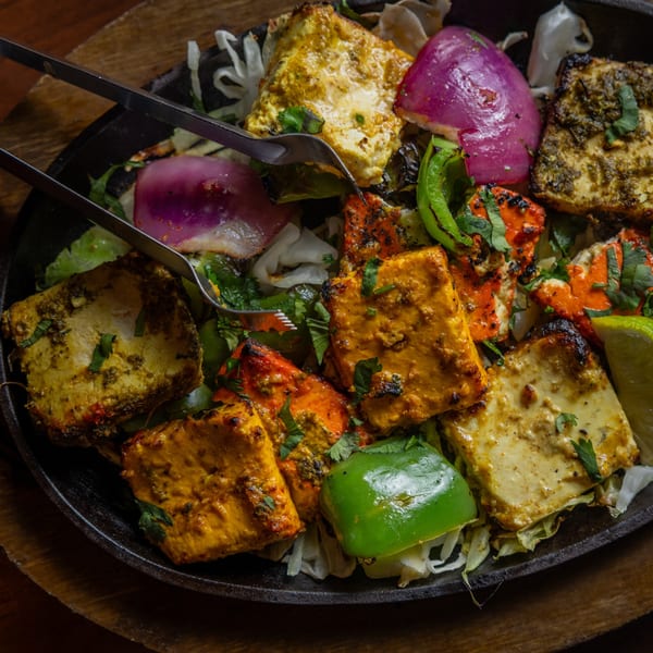 Sizzling paneer tikka with red onions, green peppers, and cilantro in a cast iron pan.