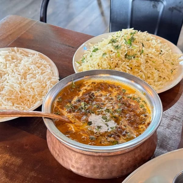 A copper pot of creamy dal makhani with two plates of rice on a wooden table.