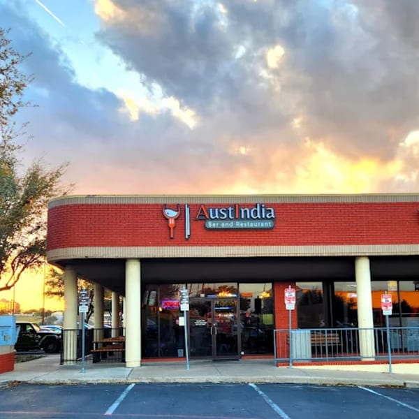 Exterior of AustIndia Bar and Restaurant with a red brick facade under a cloudy sunset sky.