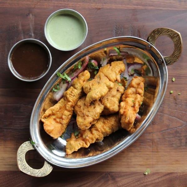 Golden fried pakoras with red onion slices and cilantro, served with green and brown dipping sauces.
