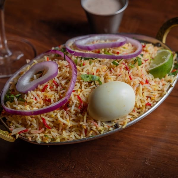 Biryani rice with red onions, a hard-boiled egg, and lime in a metal serving dish.