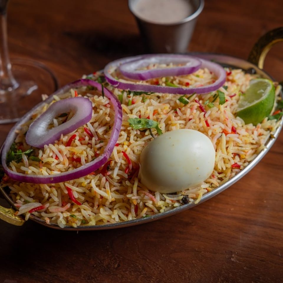 Biryani rice with red onions, a hard-boiled egg, and lime in a metal serving dish.