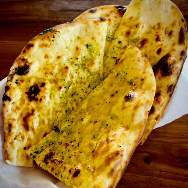 Golden naan bread, brushed with green herbs and oil, served on white paper.
