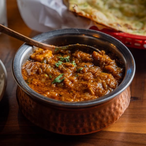 A copper bowl filled with a rich, orange-brown curry, garnished with fresh cilantro, on a wooden table.