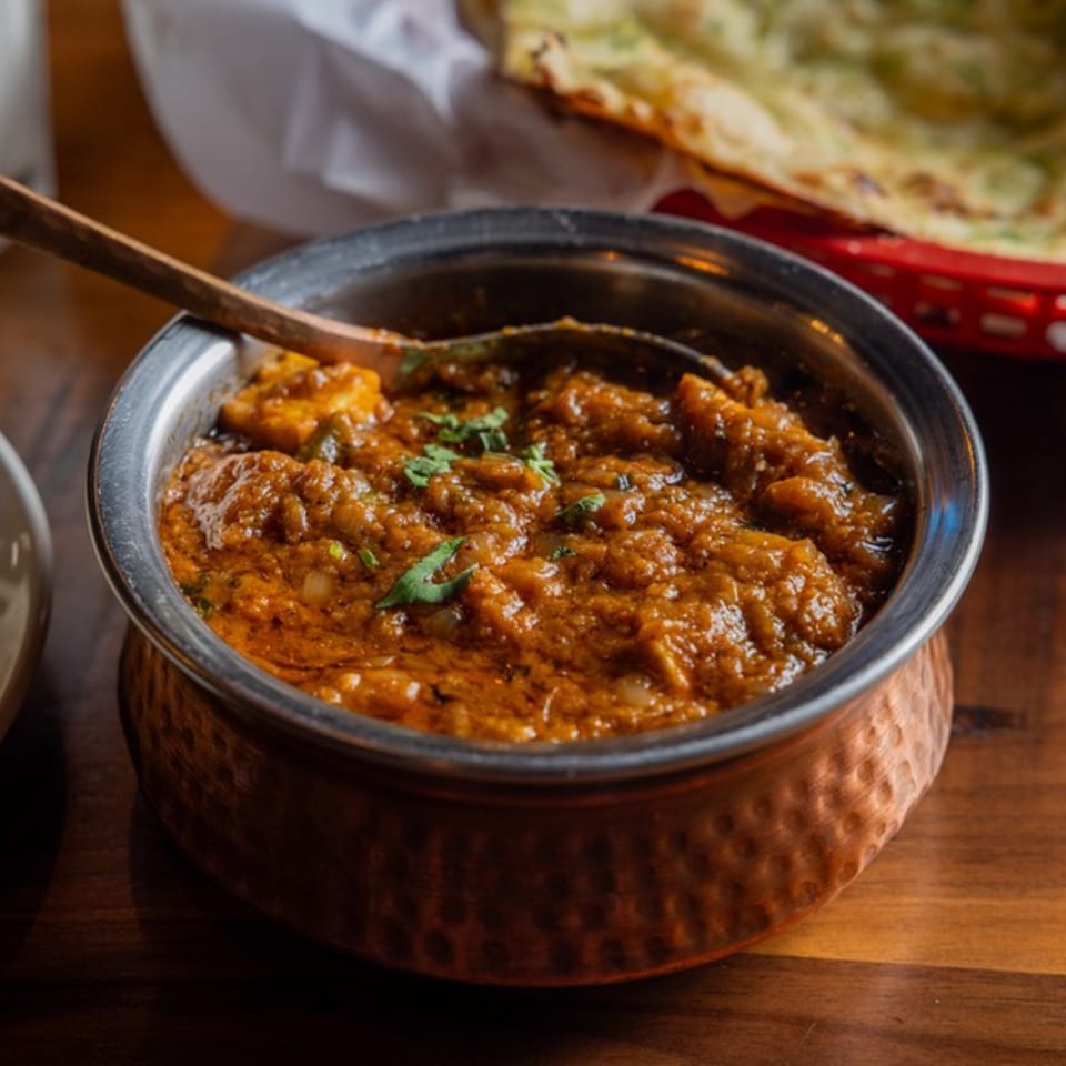 A copper bowl filled with a rich, orange-brown curry, garnished with fresh cilantro, on a wooden table.