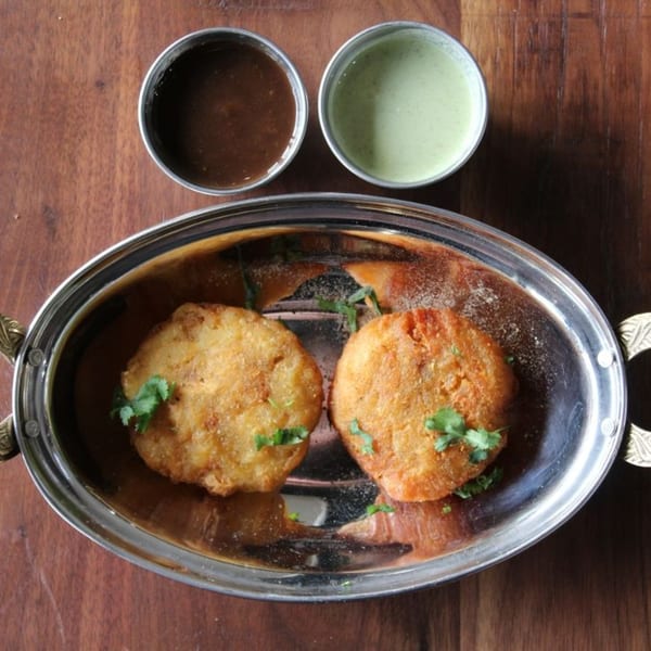 Two golden-brown fried patties garnished with cilantro in a silver dish, with two dipping sauces.