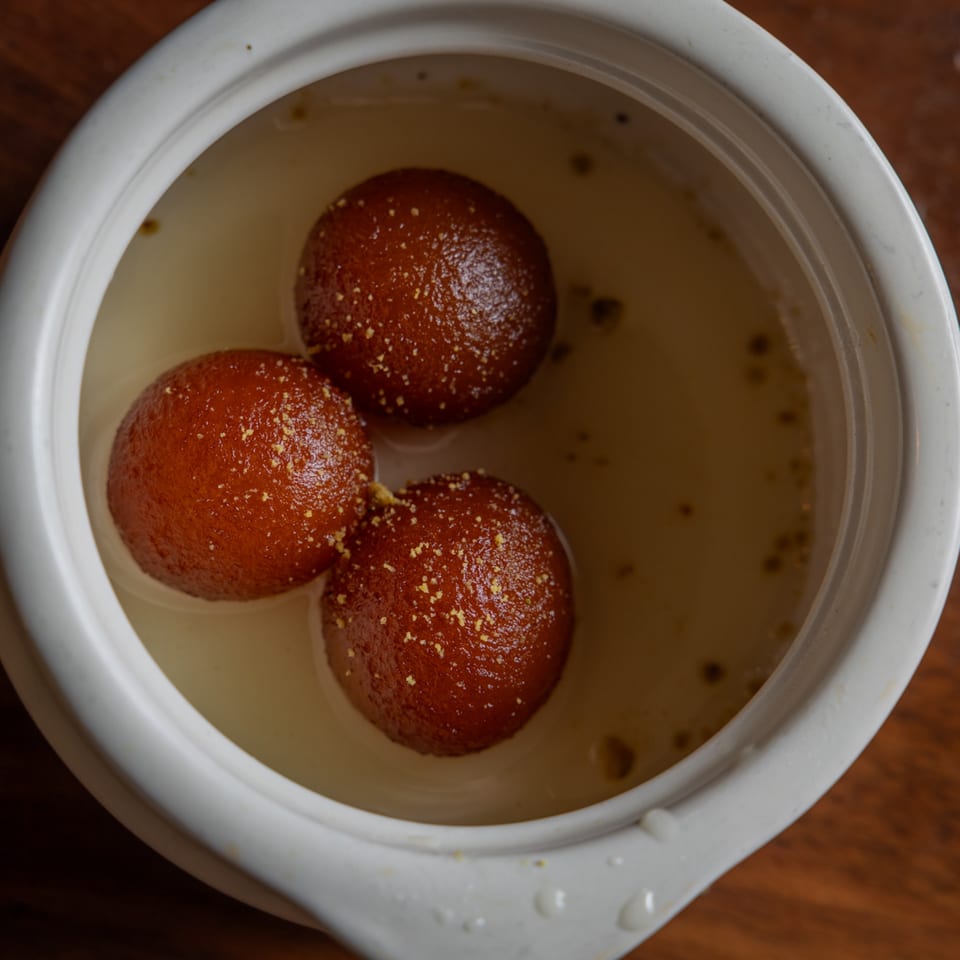 Three gulab jamuns, a traditional Indian dessert, in a white bowl filled with syrup.